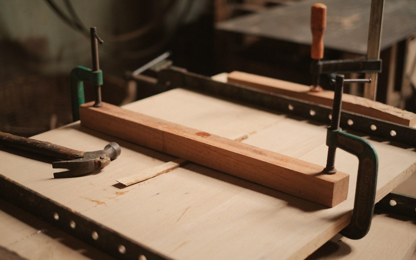 Wooden chair joint held by metal clamps on a workbench with a hammer nearby