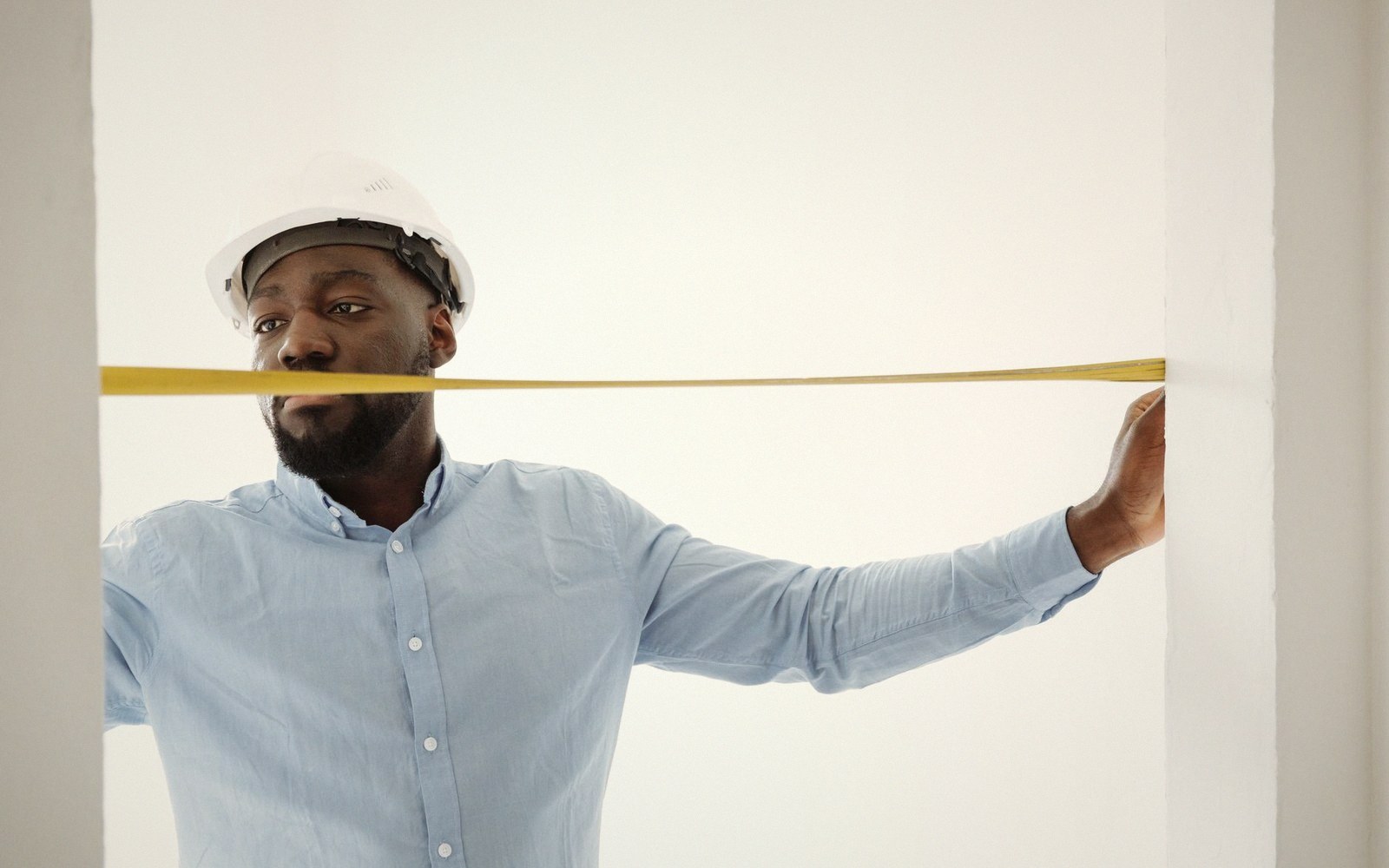 Man in a hard hat stretches a yellow tape measure across a doorway opening