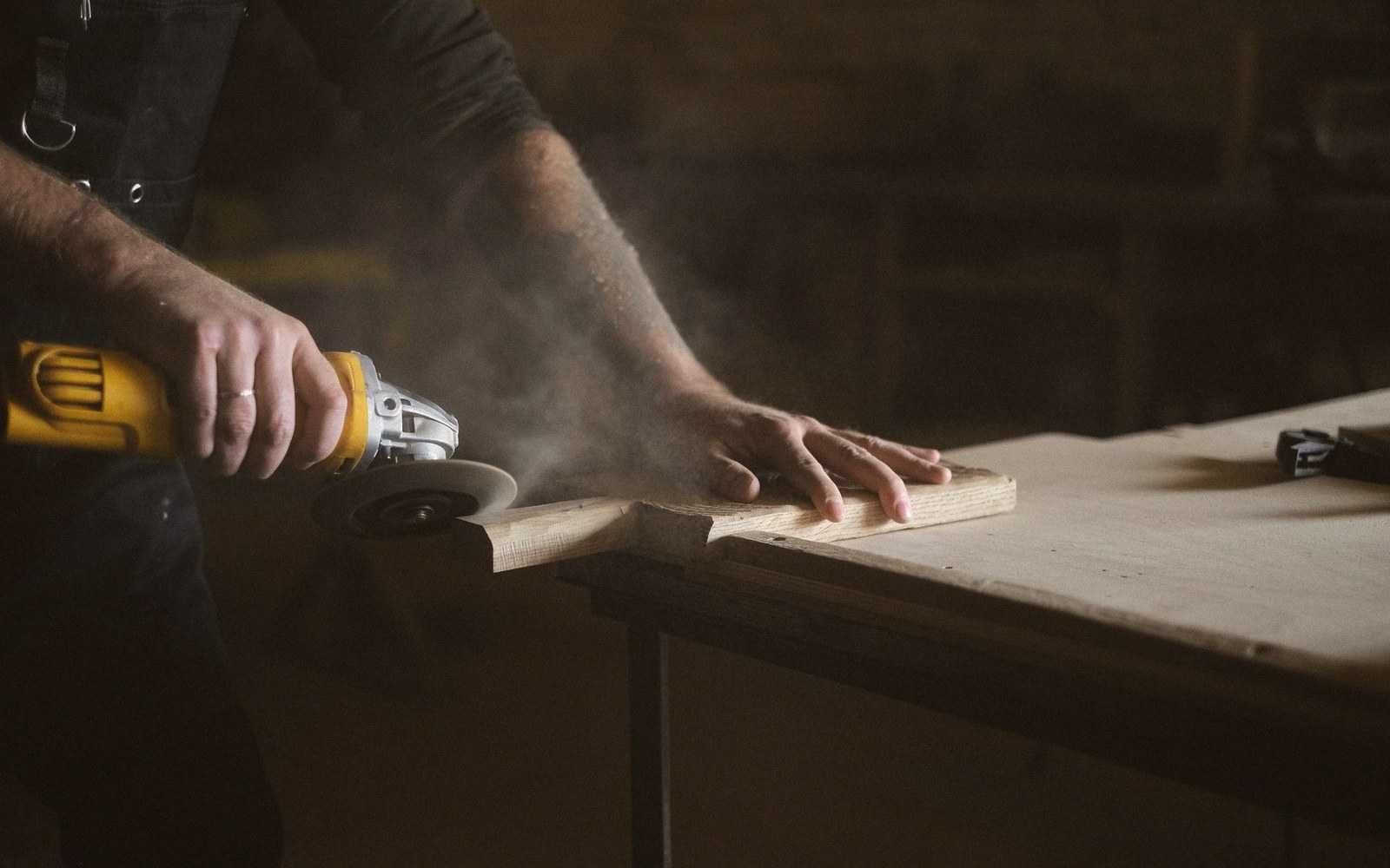 A woodworker uses an angle grinder to sand a wooden board on a workbench
