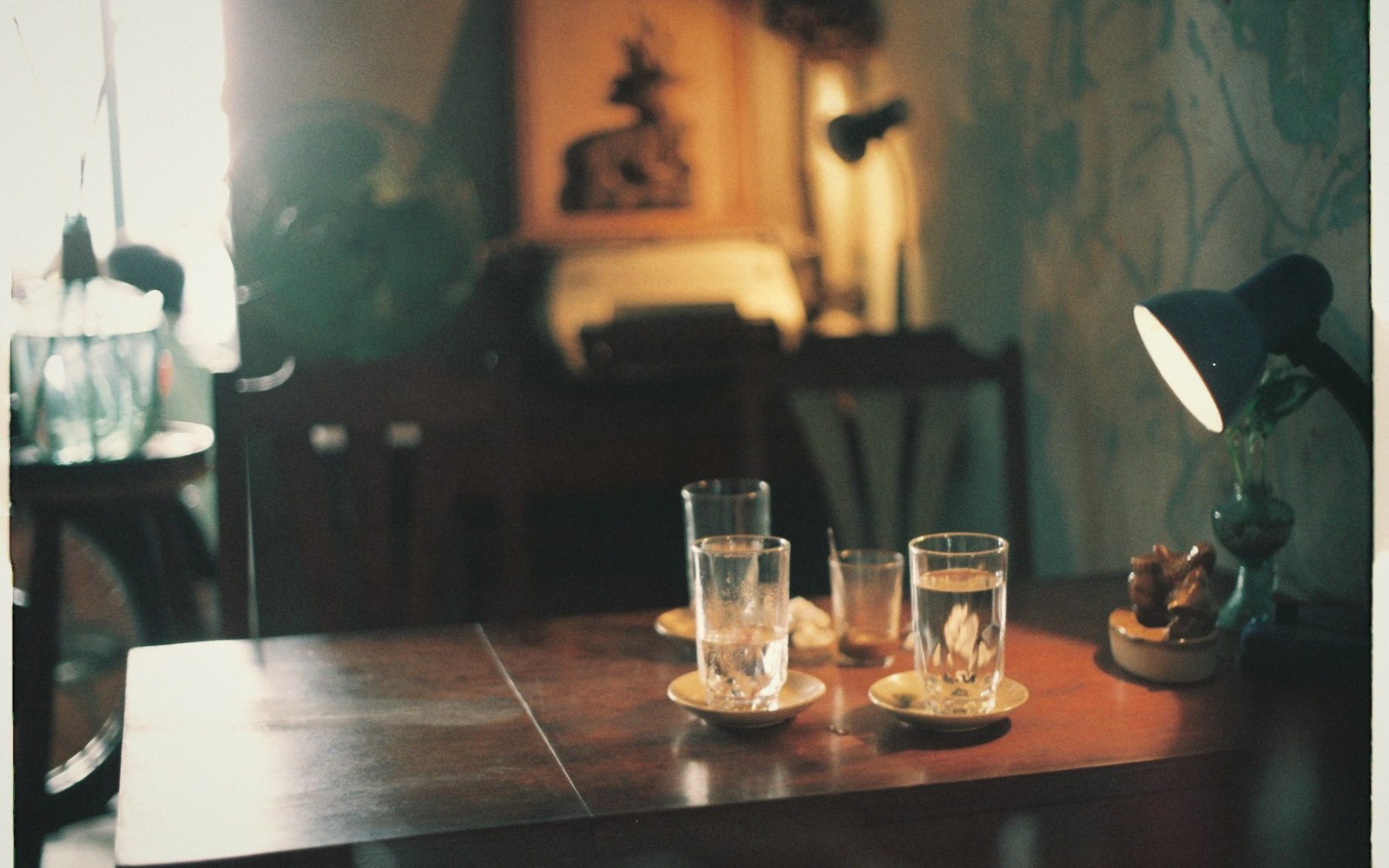 Glasses of water on saucers atop a wooden table lit by a small desk lamp