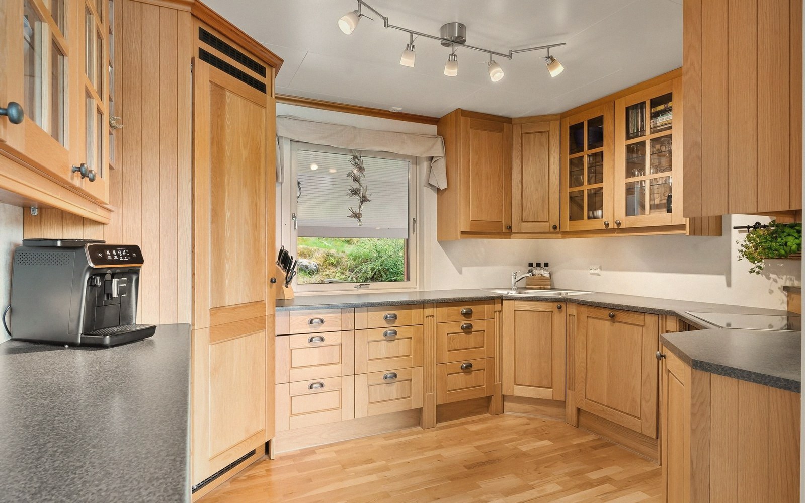 Wooden kitchen with L-shaped counters, glass-front cabinets and a window above the sink